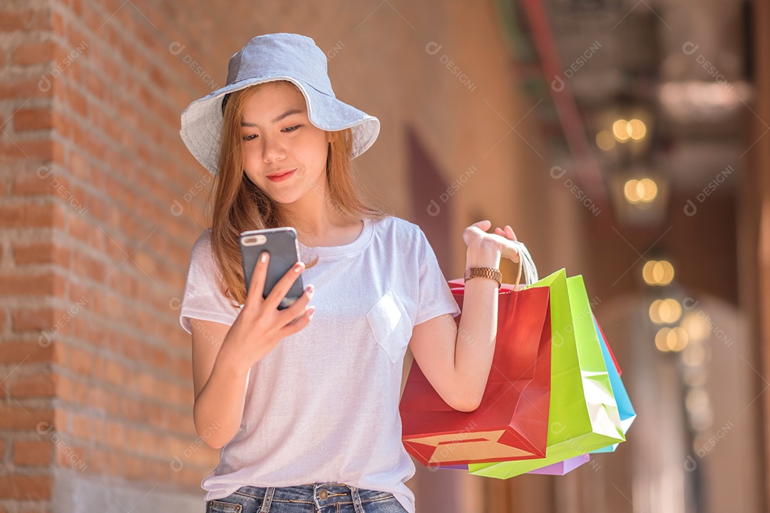 Jovem mulher usando smartphone com uma sacola de compras na outra mão, conceitos de compras.