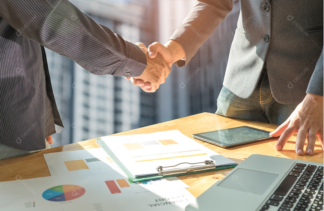 Conceito de negócio, dois homens apertam as mãos com documentos e laptops colocados na mesa, o fundo é um condomínio.