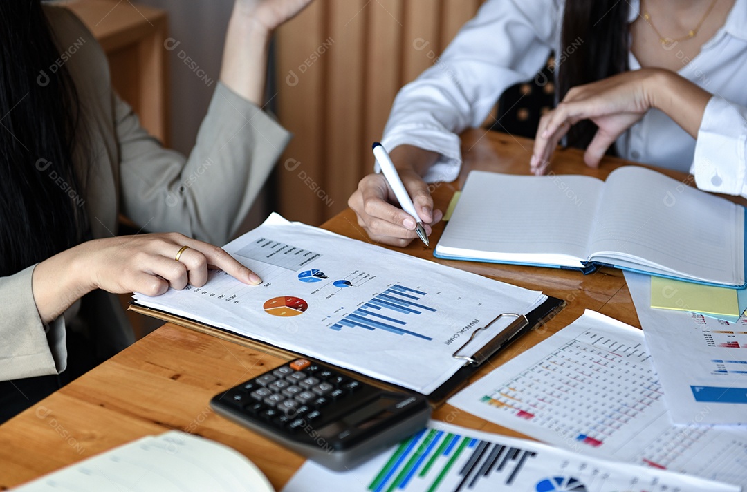 Escritório de duas garotas está analisando gráficos na mesa. Eles apontam os dedos para o gráfico e seguram a caneta na mão.