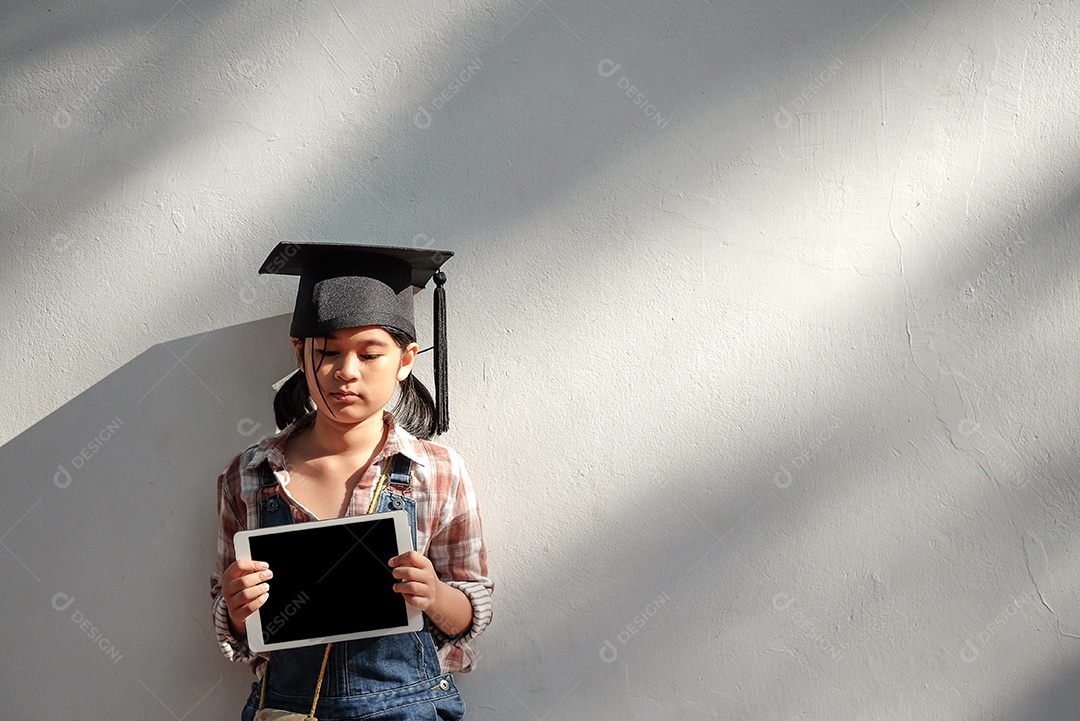 Menina usam um chapéu de formatura segurando um tablet na mão, frente do tablet e suporte de parede.