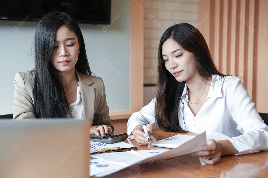 Duas mulheres jovens estão discutindo o trabalho na sala de conferências. Laptop e documento na mesa.