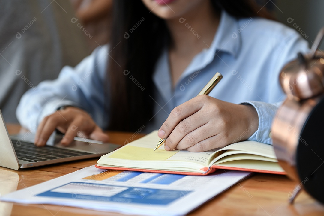 Trabalhadoras de escritório femininas usando laptop e escrevendo notas.