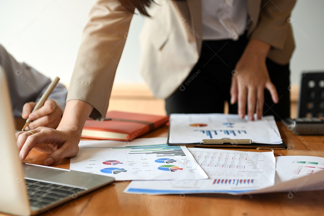 Trabalhadores de escritório feminino estão analisando dados de gráficos. Eles usam uma calculadora e um laptop.