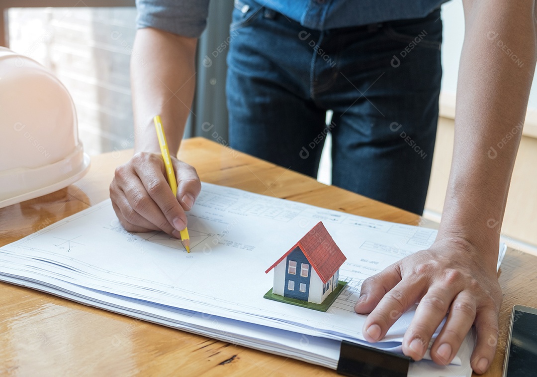 Arquiteto segurando uma planta de desenho de lápis amarelo com casa modelo na planta baixa.