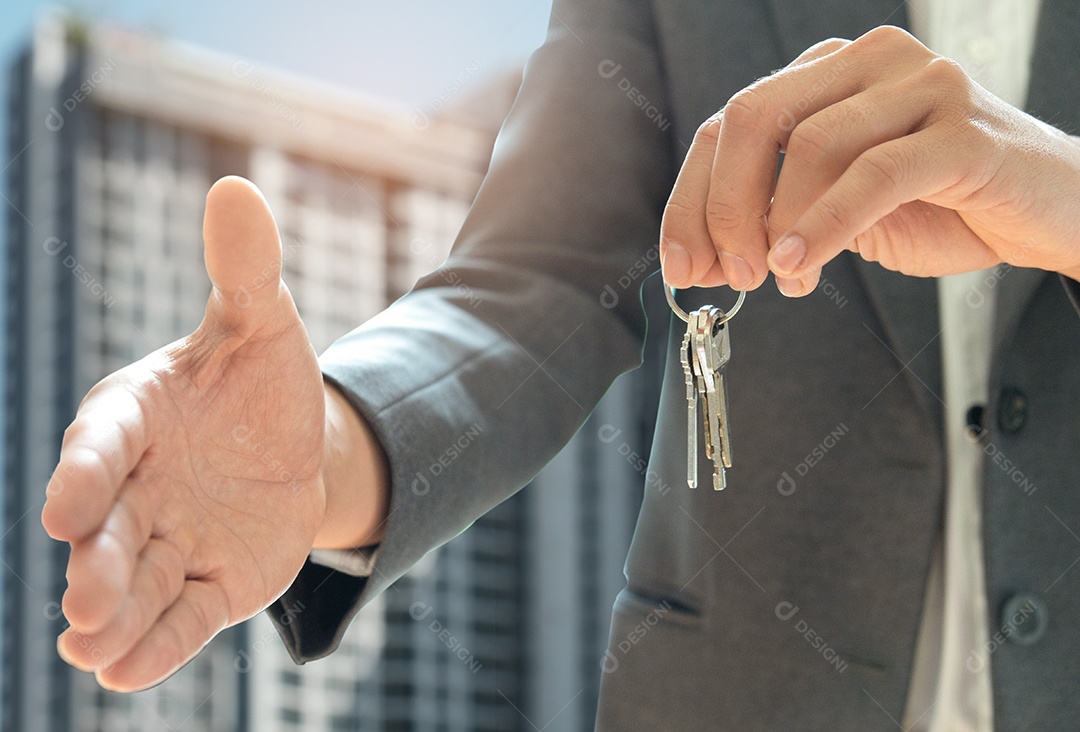 Vendas de casa apertam a mão e a outra mão segura a chave da casa. O plano de fundo é uma convenção.
