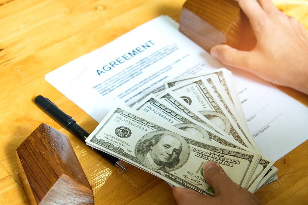 Conceito de compra de casa, dólares e casas modelo com documentos de acordo na mesa.