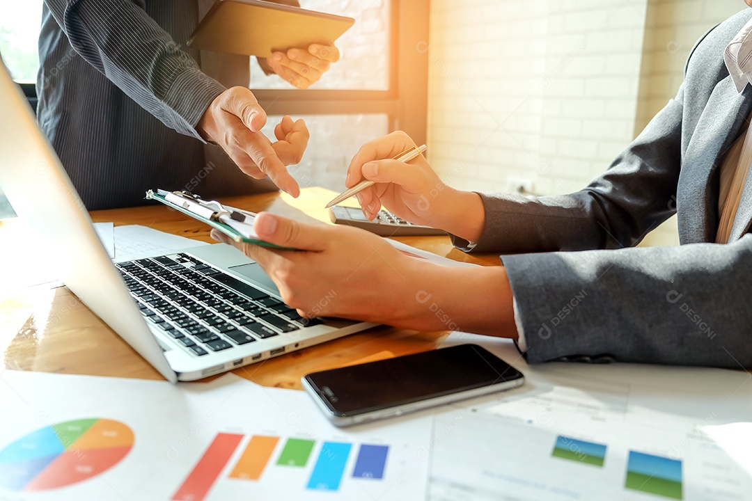 Equipe de negócios usa um tablet para analisar dados. Na mesa estão gráficos e laptops.