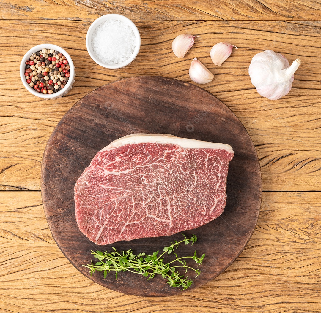 Carne assada de ombro wagyu crua sobre tábua de madeira com temperos.