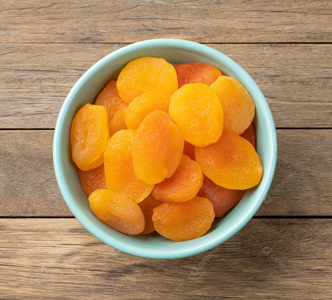 Damascos secos em uma tigela sobre a mesa de madeira.