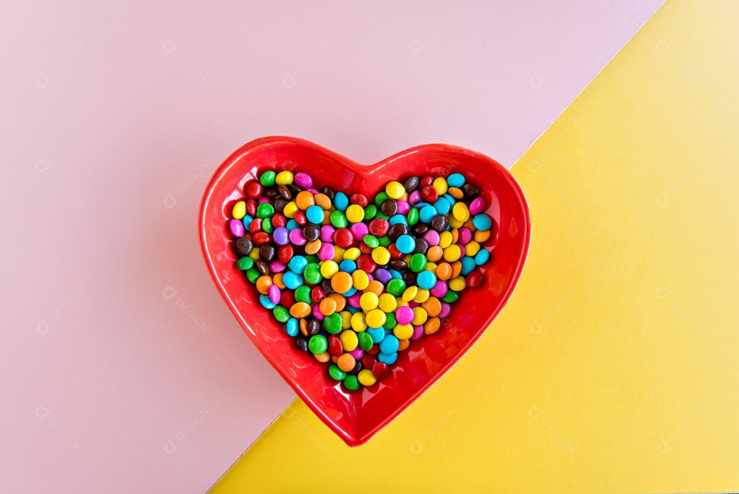 Chocolates de confete no prato em forma de coração em amarelo e rosa bac