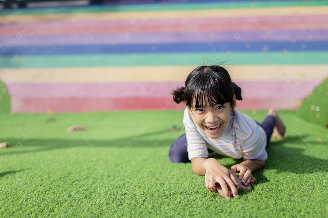 Linda garota asiática se divertindo tentando escalar pedras artificiais no pátio da escola, menina subindo a parede de pedra, coordenação