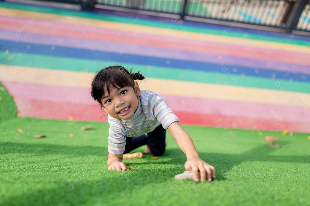 Linda garota asiática se divertindo tentando escalar pedras artificiais no pátio da escola, menina subindo a parede de pedra, coordenação
