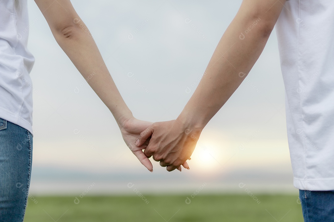 Casal de mãos dadas em campo verde no pôr do sol