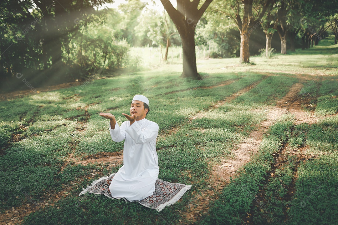 Homem muçulmano religioso tradicional kandura orando ao ar livre em raios de sol de ambiente de natureza tranquila.