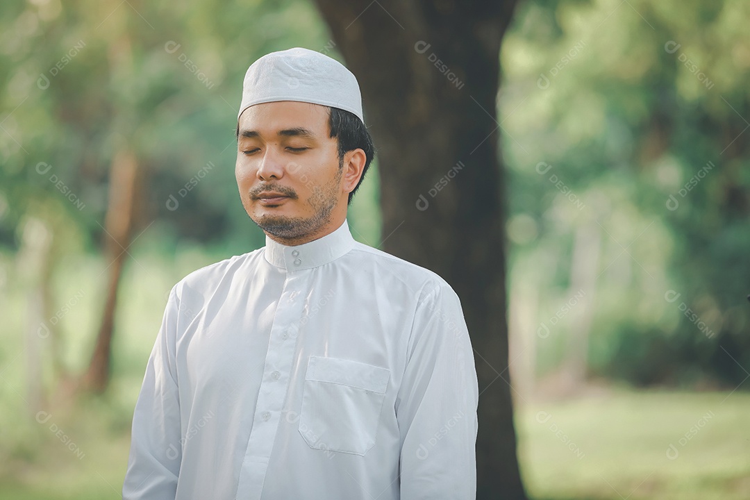Homem muçulmano religioso tradicional kandura orando ao ar livre em raios de sol de ambiente de natureza tranquila.