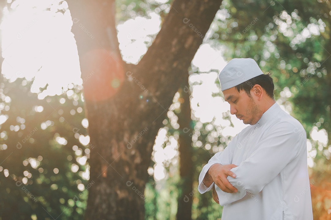 Homem muçulmano religioso tradicional kandura orando ao ar livre em raios de sol de ambiente de natureza tranquila.