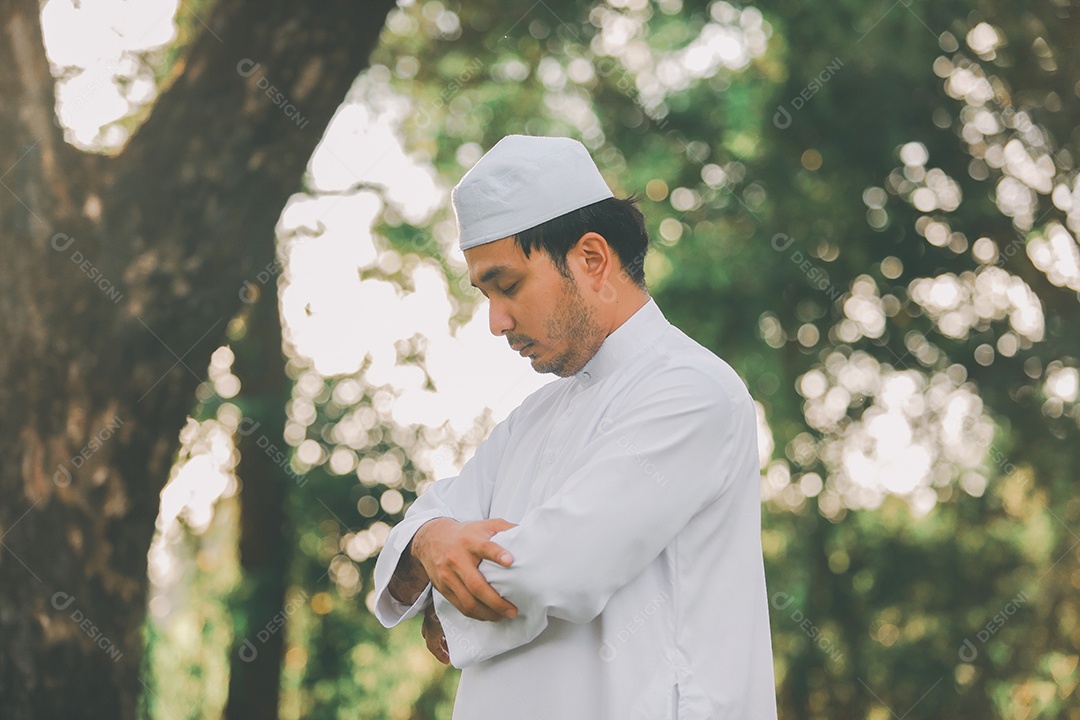 Homem muçulmano religioso tradicional kandura orando ao ar livre em raios de sol de ambiente de natureza tranquila.