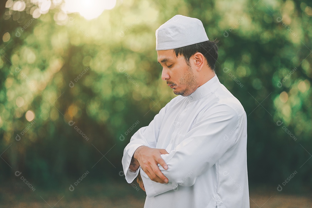 Homem muçulmano religioso tradicional kandura orando ao ar livre em raios de sol de ambiente de natureza tranquila.