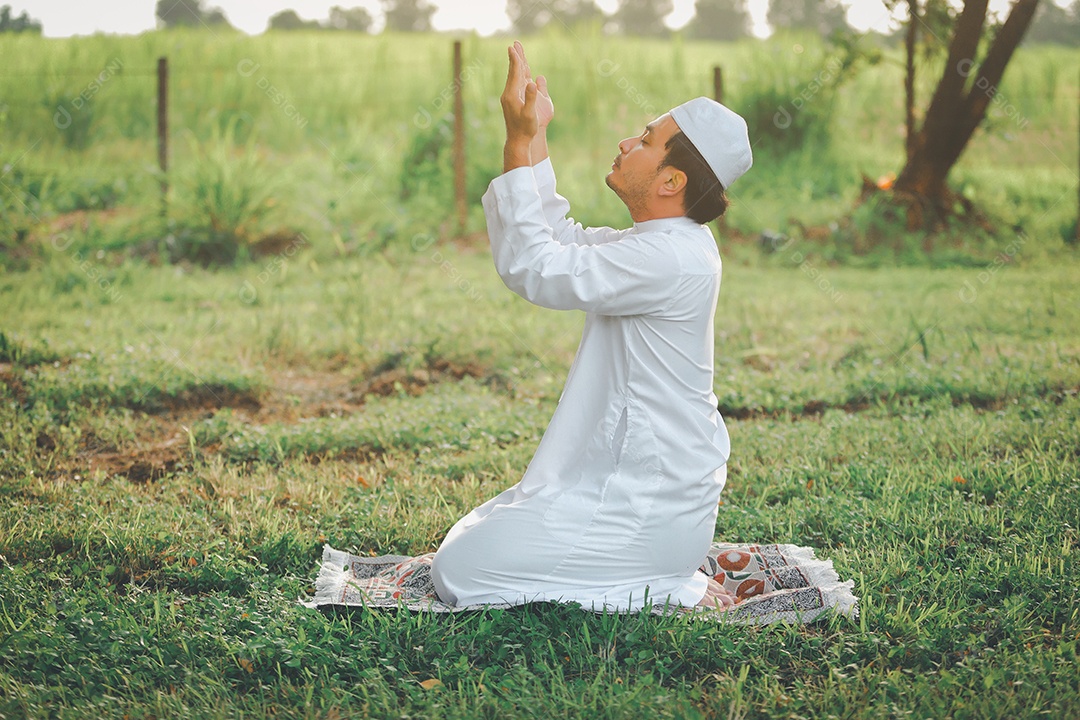 Homem muçulmano religioso tradicional kandura orando ao ar livre em raios de sol de ambiente de natureza tranquila.