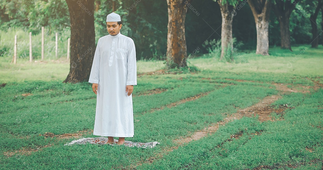 Homem muçulmano religioso tradicional kandura orando ao ar livre em raios de sol de ambiente de natureza tranquila.