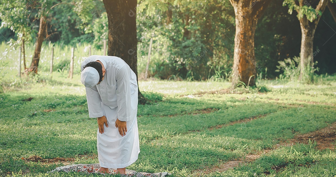 Homem muçulmano religioso tradicional kandura orando ao ar livre em raios de sol de ambiente de natureza tranquila.