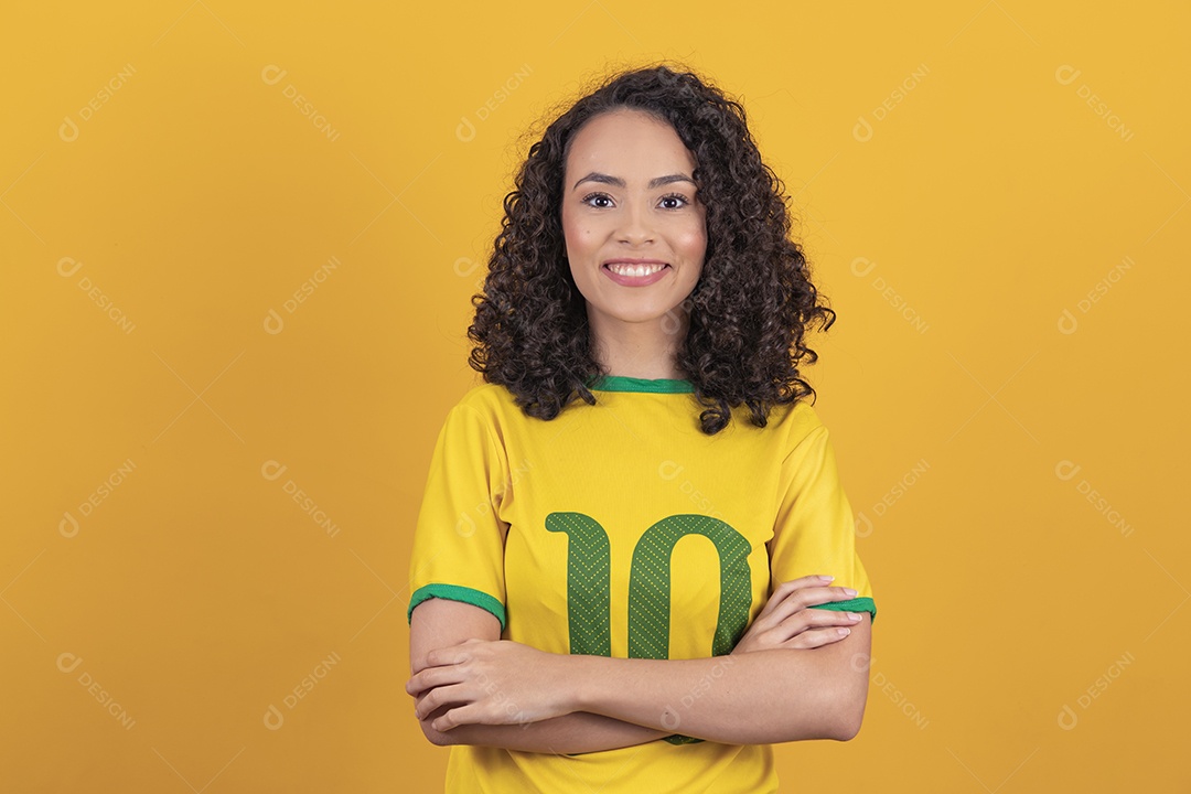 Mulher jovem usando camiseta da seleção brasileira futebol cabelo cacheado sobre fundo amarelo