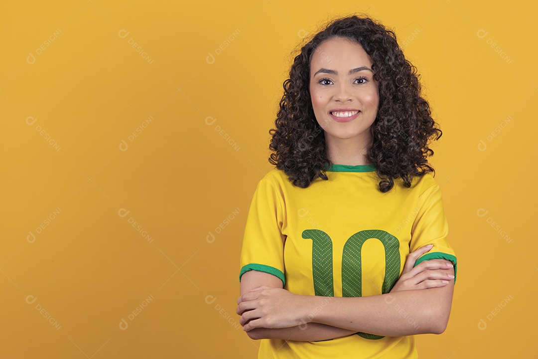 Mulher jovem usando camiseta da seleção brasileira futebol cabelo cacheado sobre fundo amarelo