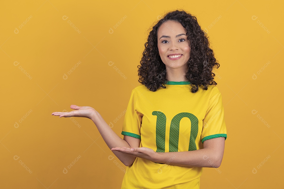 Mulher jovem usando camiseta da seleção brasileira futebol cabelo cacheado sobre fundo amarelo