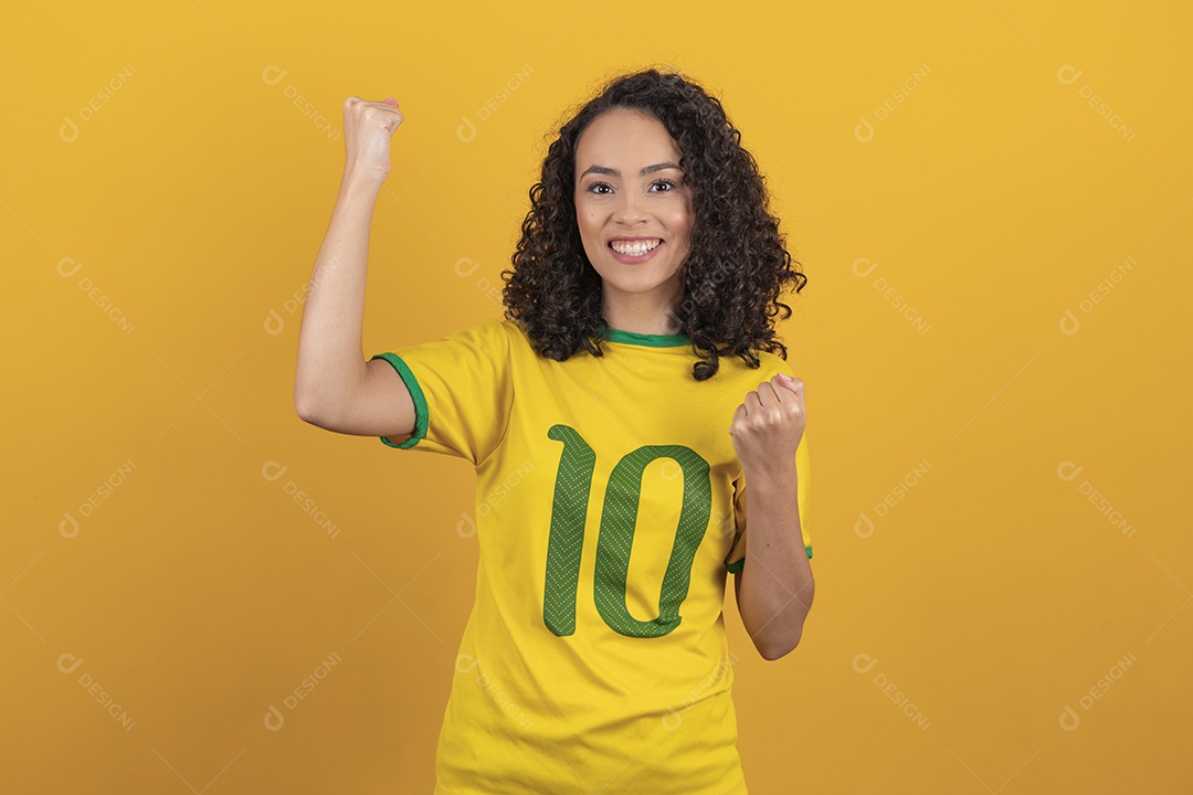 Mulher jovem usando camiseta da seleção brasileira futebol cabelo cacheado sobre fundo amarelo