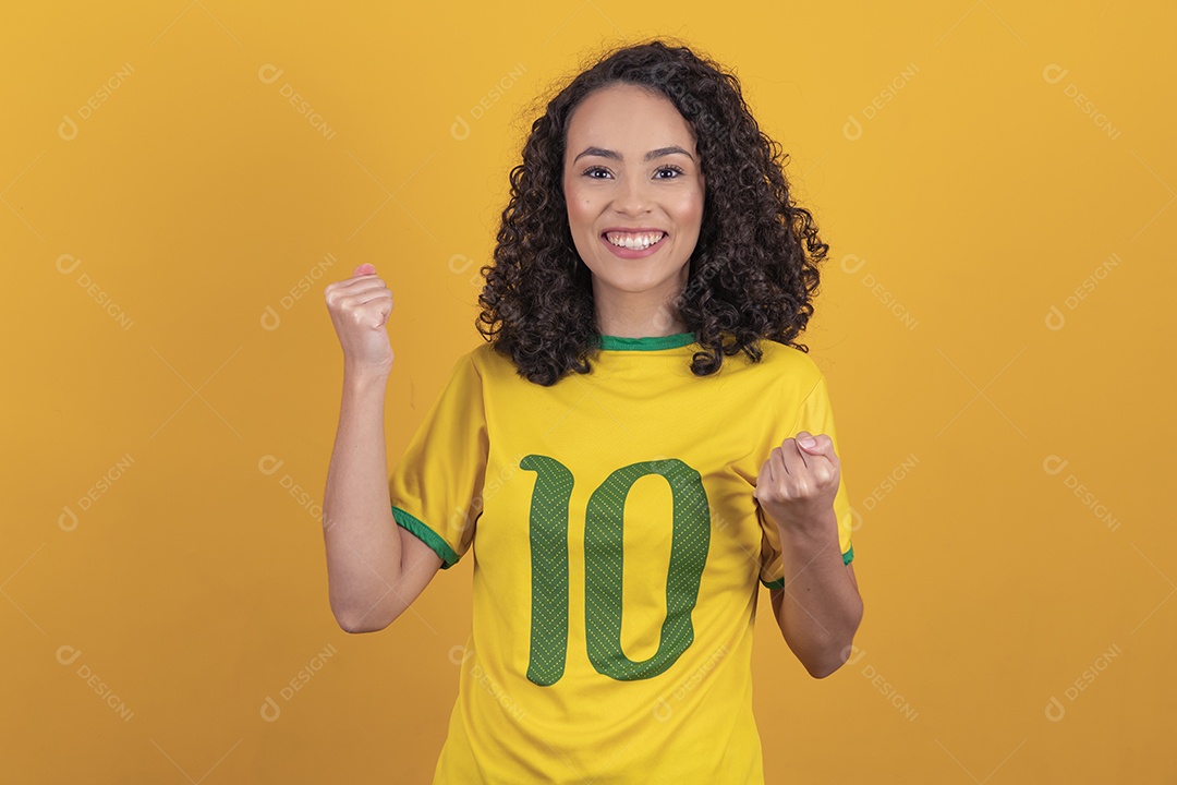 Mulher jovem usando camiseta da seleção brasileira futebol cabelo cacheado sobre fundo amarelo
