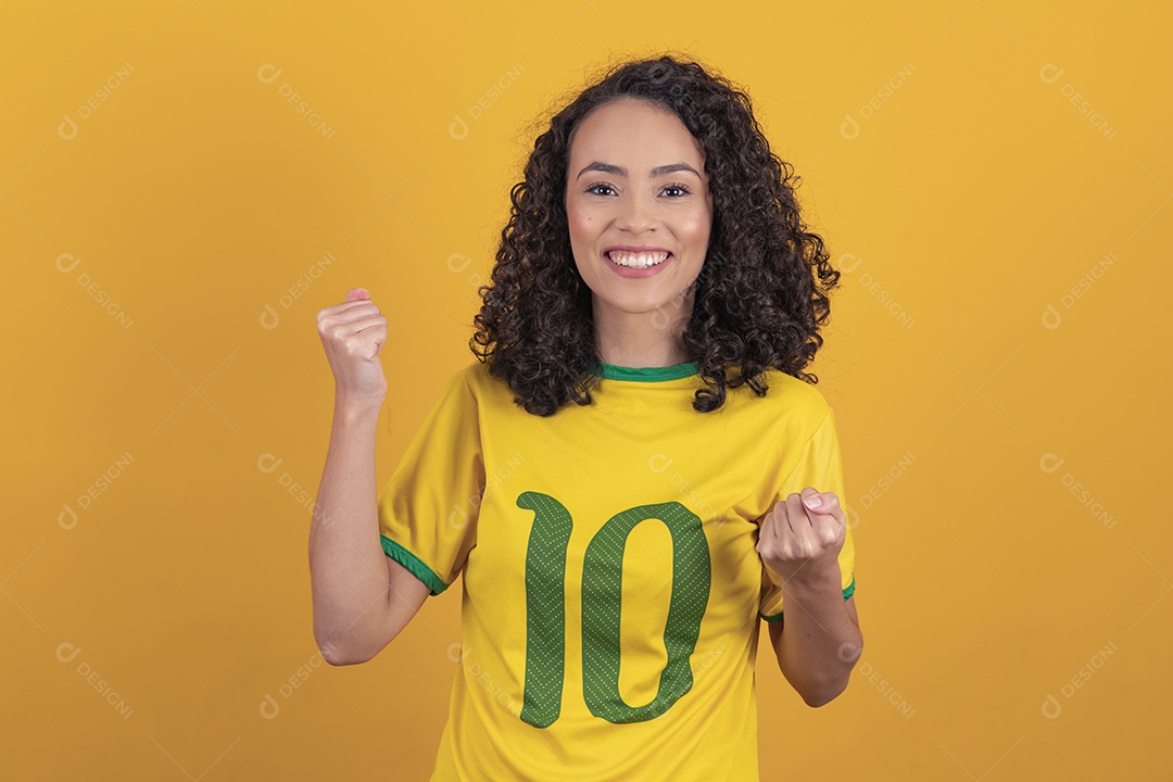 Mulher jovem usando camiseta da seleção brasileira futebol cabelo cacheado sobre fundo amarelo