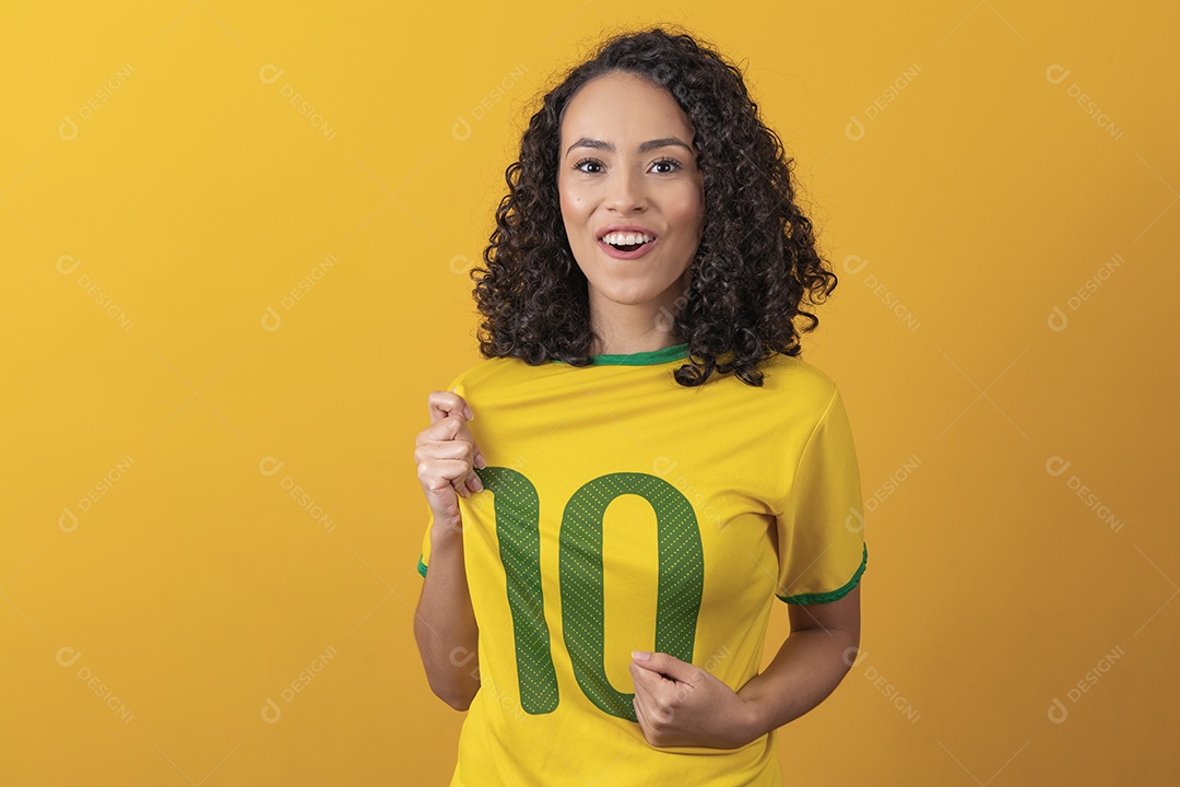 Mulher jovem usando camiseta da seleção brasileira futebol cabelo cacheado sobre fundo amarelo