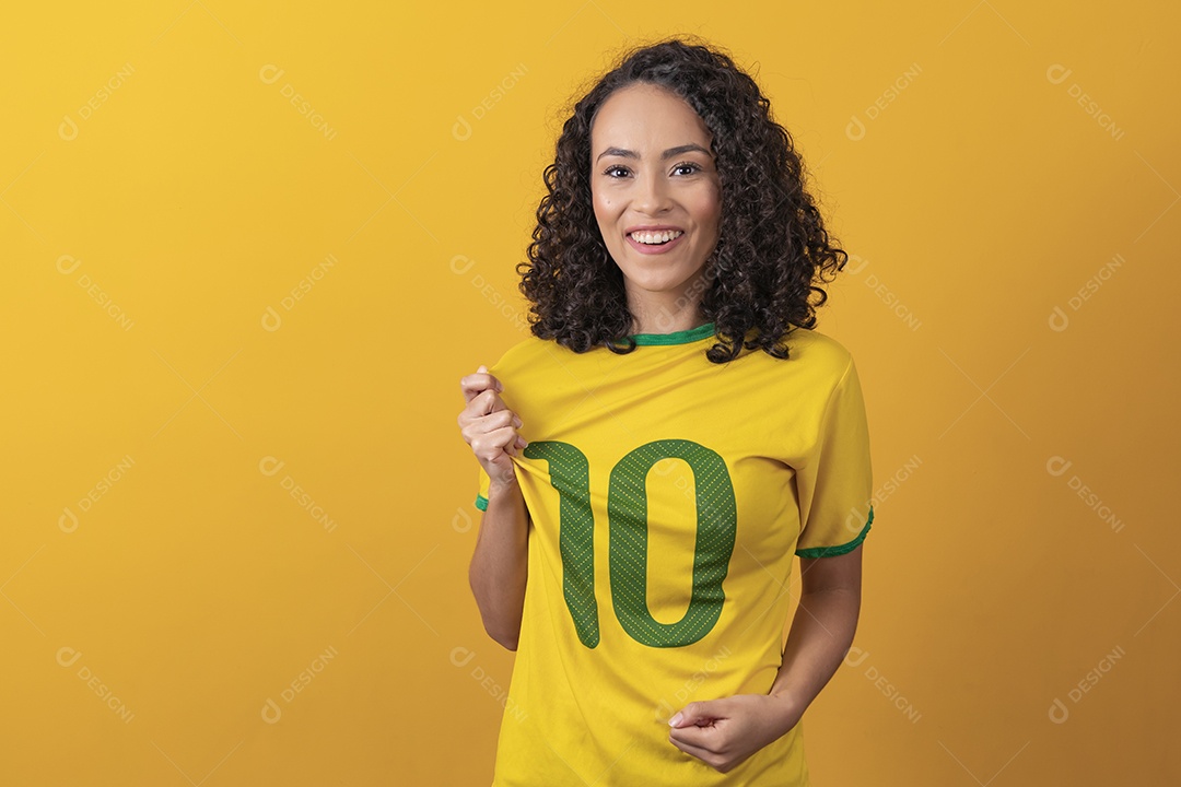 Mulher jovem usando camiseta da seleção brasileira futebol cabelo cacheado sobre fundo amarelo