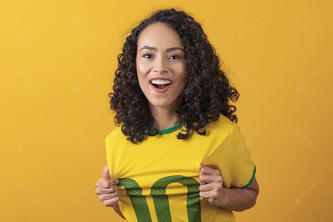 Mulher jovem usando camiseta da seleção brasileira futebol cabelo cacheado sobre fundo amarelo