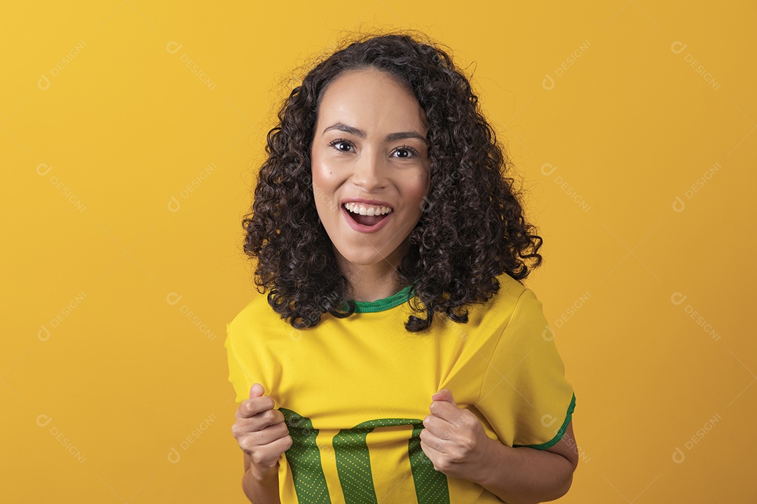 Mulher jovem usando camiseta da seleção brasileira futebol cabelo cacheado sobre fundo amarelo