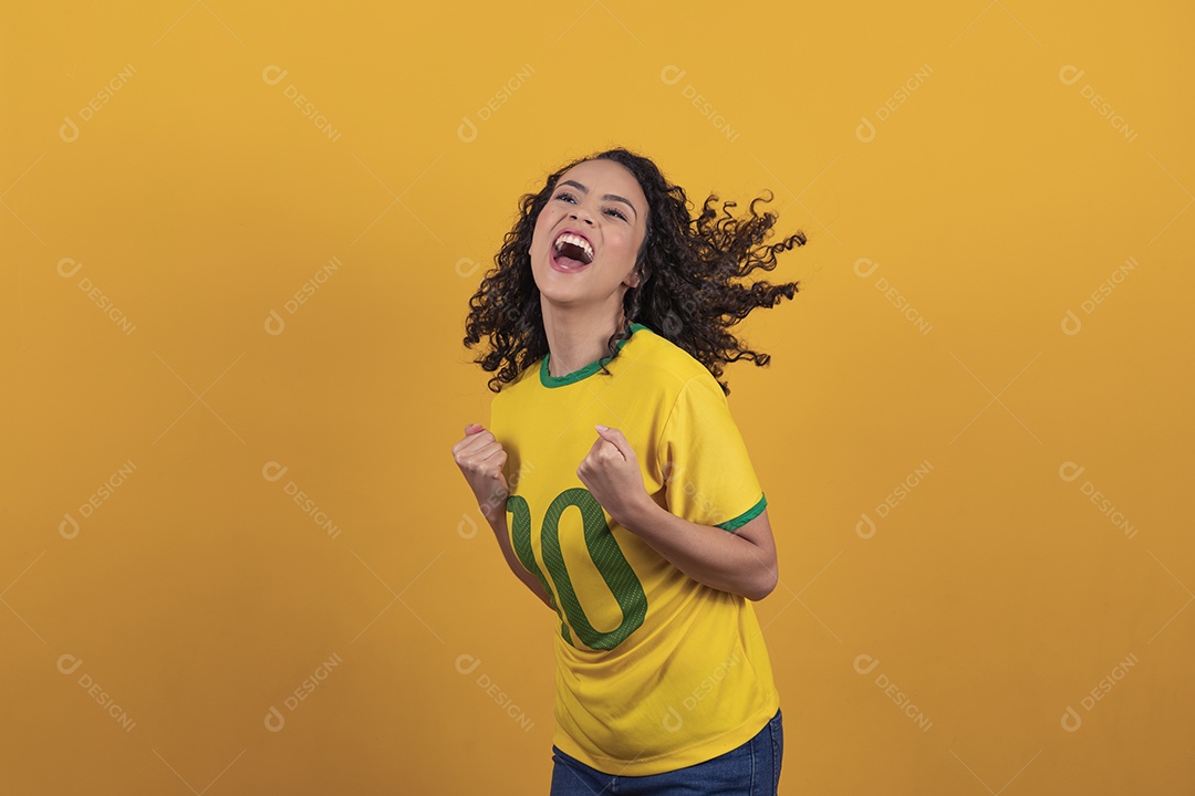 Mulher jovem usando camiseta da seleção brasileira futebol cabelo cacheado sobre fundo amarelo