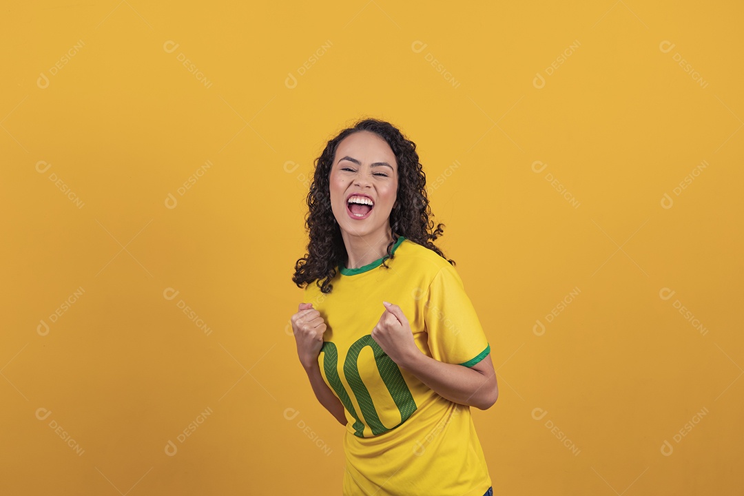 Mulher jovem usando camiseta da seleção brasileira futebol cabelo cacheado sobre fundo amarelo