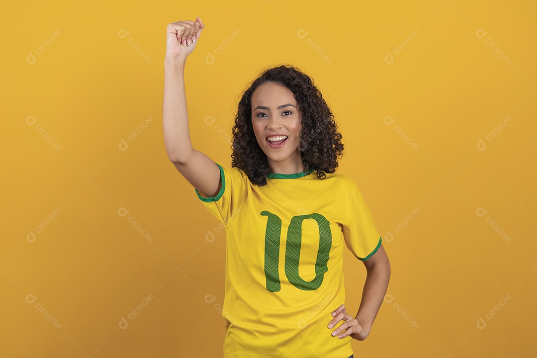 Mulher jovem usando camiseta da seleção brasileira futebol cabelo cacheado sobre fundo amarelo