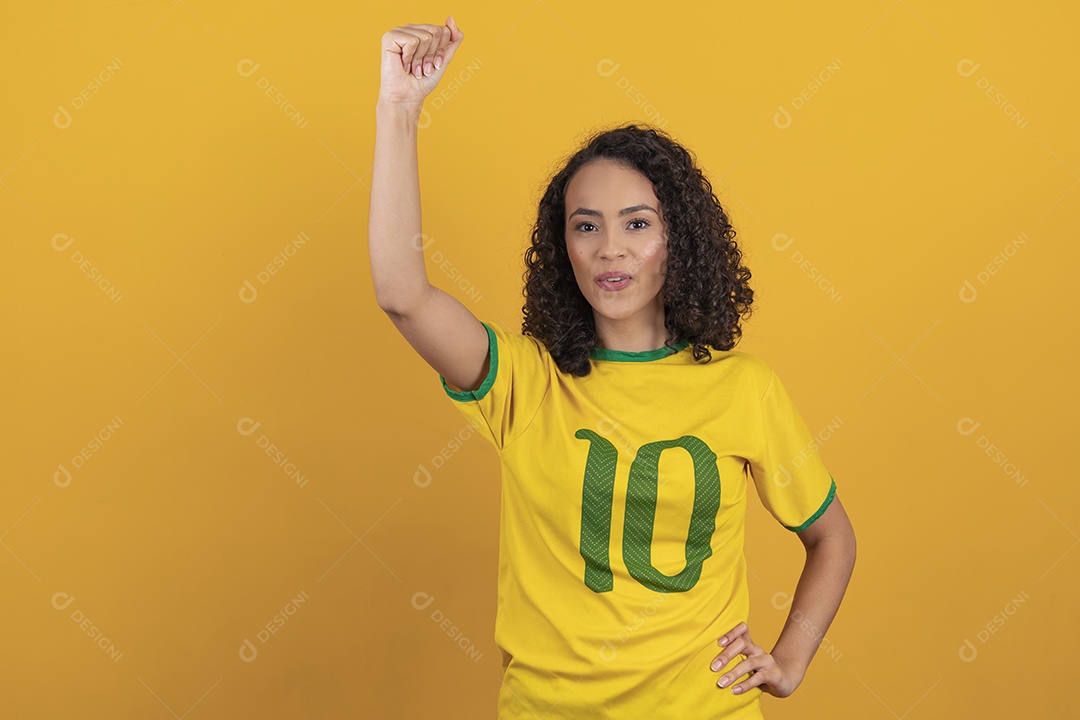 Mulher jovem usando camiseta da seleção brasileira futebol cabelo cacheado sobre fundo amarelo