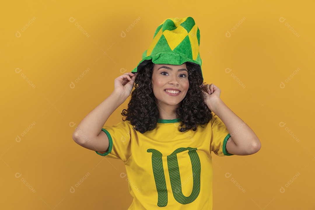 Mulher jovem usando camiseta da seleção brasileira futebol cabelo cacheado sobre fundo amarelo