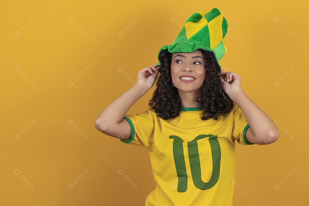 Mulher jovem usando camiseta da seleção brasileira futebol cabelo cacheado sobre fundo amarelo