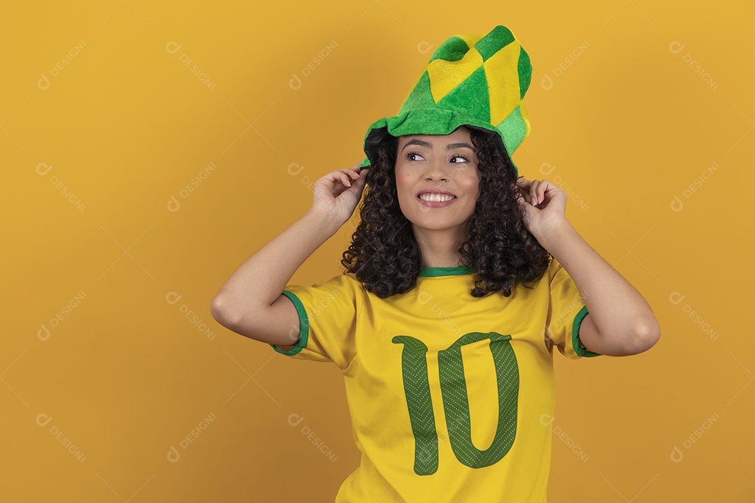 Mulher jovem usando camiseta da seleção brasileira futebol cabelo cacheado sobre fundo amarelo