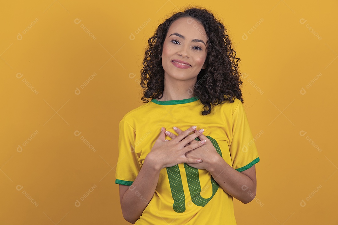 Mulher jovem usando camiseta da seleção brasileira futebol cabelo cacheado sobre fundo amarelo