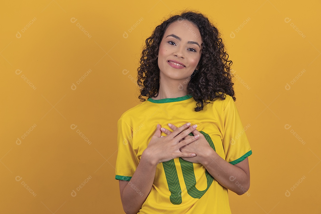 Mulher jovem usando camiseta da seleção brasileira futebol cabelo cacheado sobre fundo amarelo