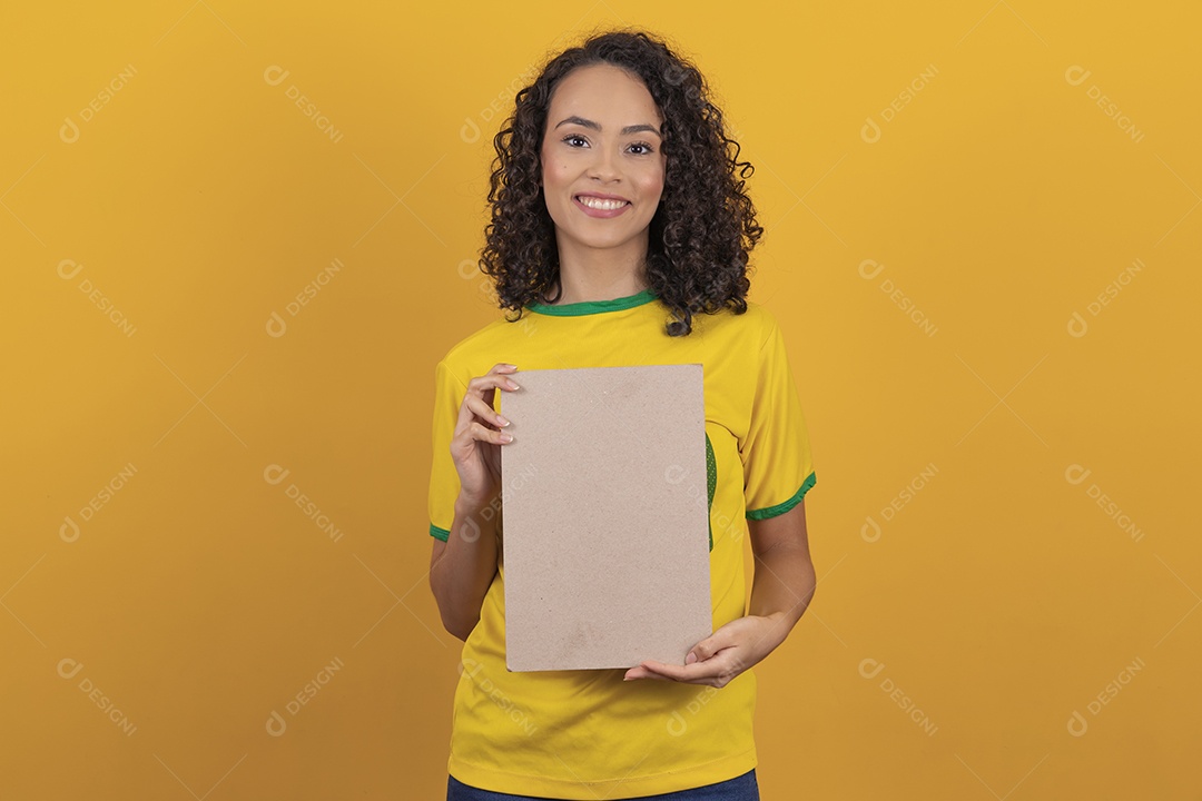 Mulher jovem usando camiseta da seleção brasileira futebol cabelo cacheado sobre fundo amarelo