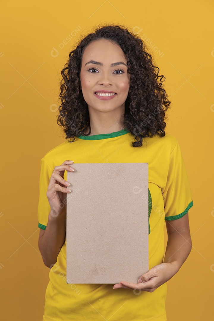 Mulher jovem usando camiseta da seleção brasileira futebol cabelo cacheado sobre fundo amarelo