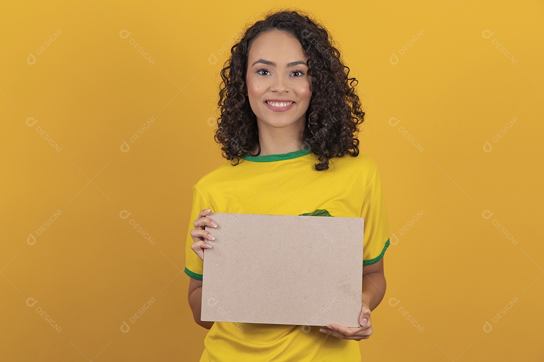 Mulher jovem usando camiseta da seleção brasileira futebol cabelo cacheado sobre fundo amarelo