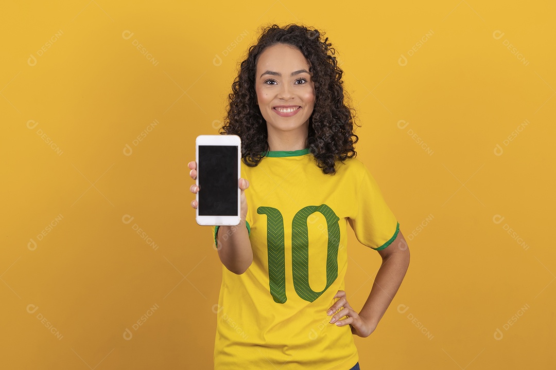 Mulher jovem usando camiseta da seleção brasileira futebol cabelo cacheado sobre fundo amarelo