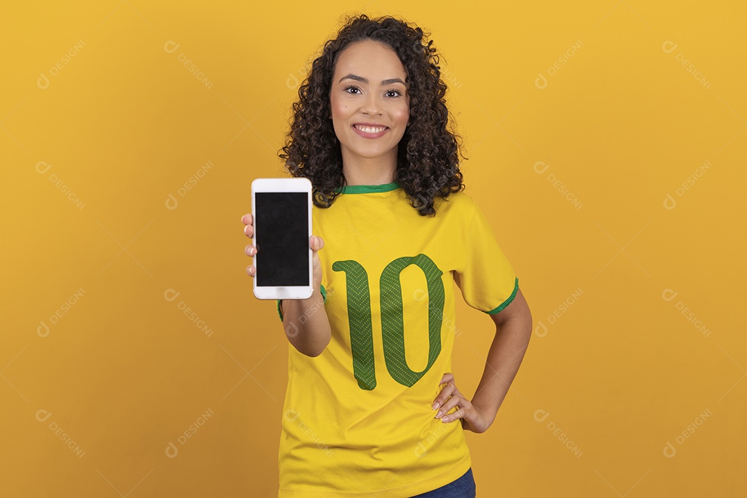 Mulher jovem usando camiseta da seleção brasileira futebol cabelo cacheado sobre fundo amarelo