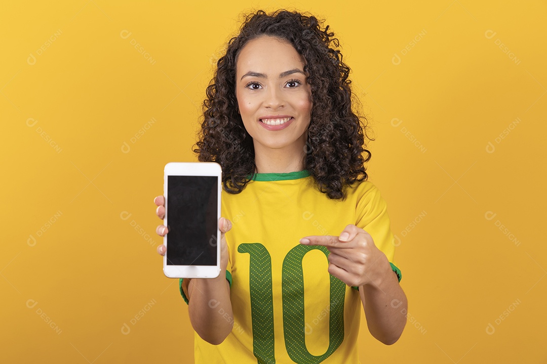 Mulher jovem usando camiseta da seleção brasileira futebol cabelo cacheado sobre fundo amarelo
